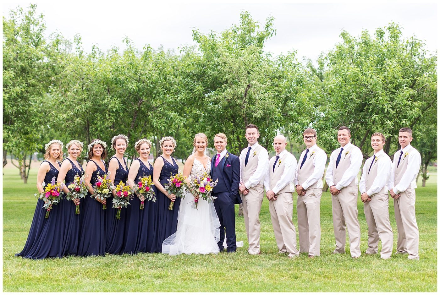 All groomsmen and bridesmaids standing with the bride and groom smiling and looking at the camera during bridal party photos