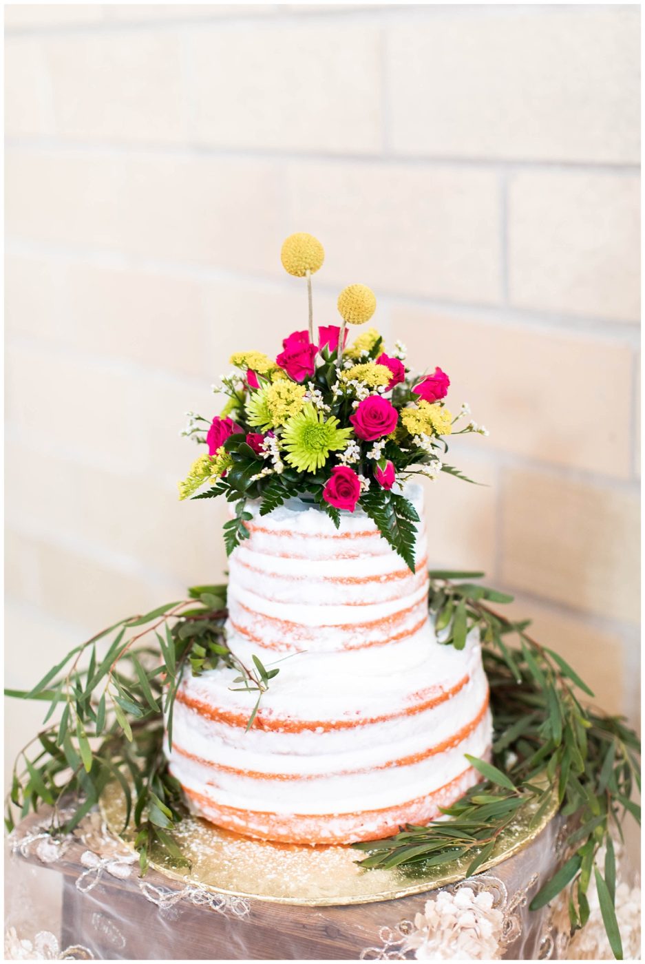 Naked 3-tier wedding cake topped with tons of wildflowers and surrounded by gorgeous greenery
