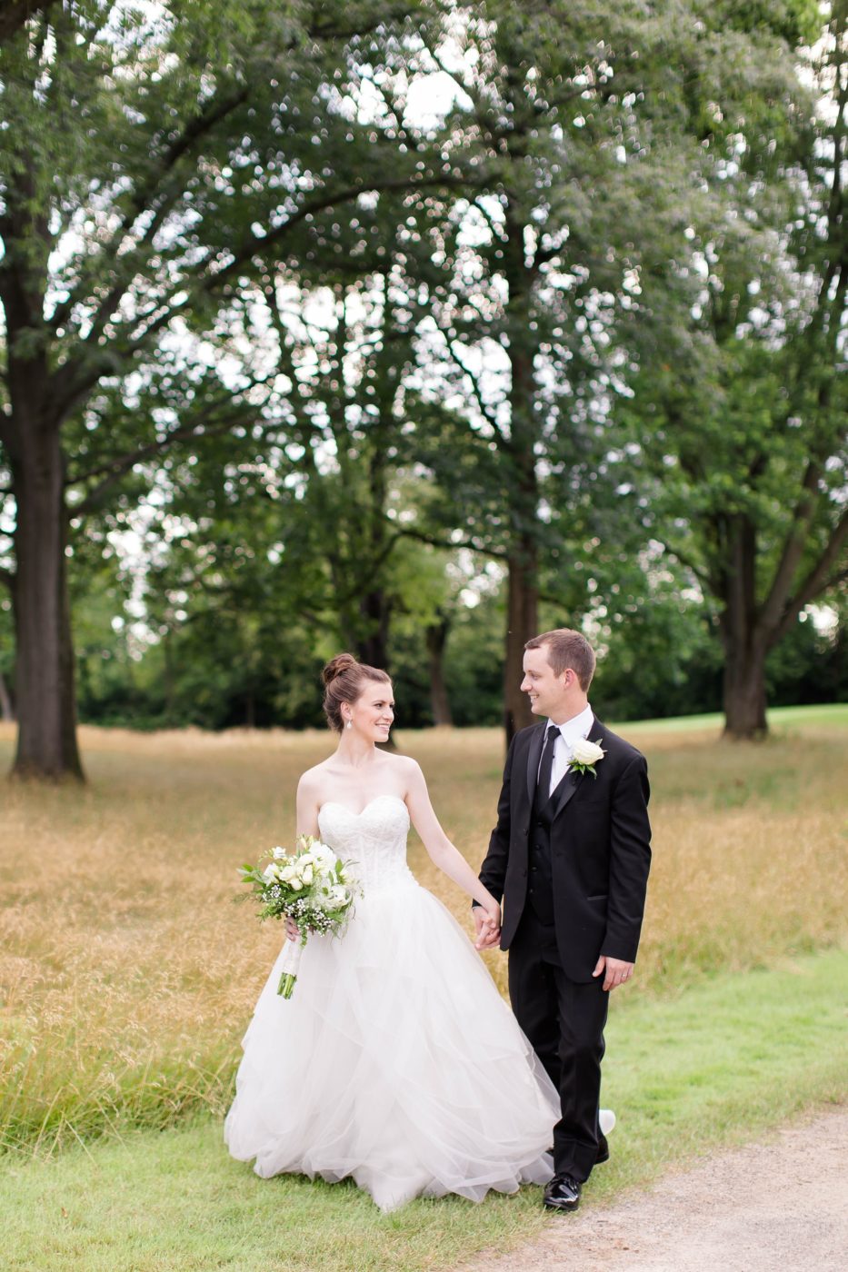 Bride and Groom holding hands while walking and laughing together in a field.