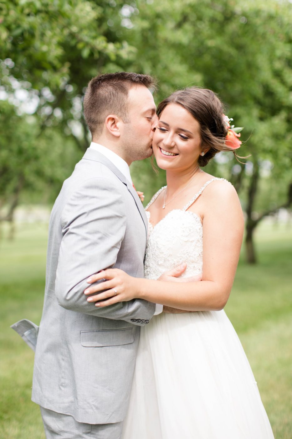 Groom holding his bride close as he gives her a kiss on the cheek