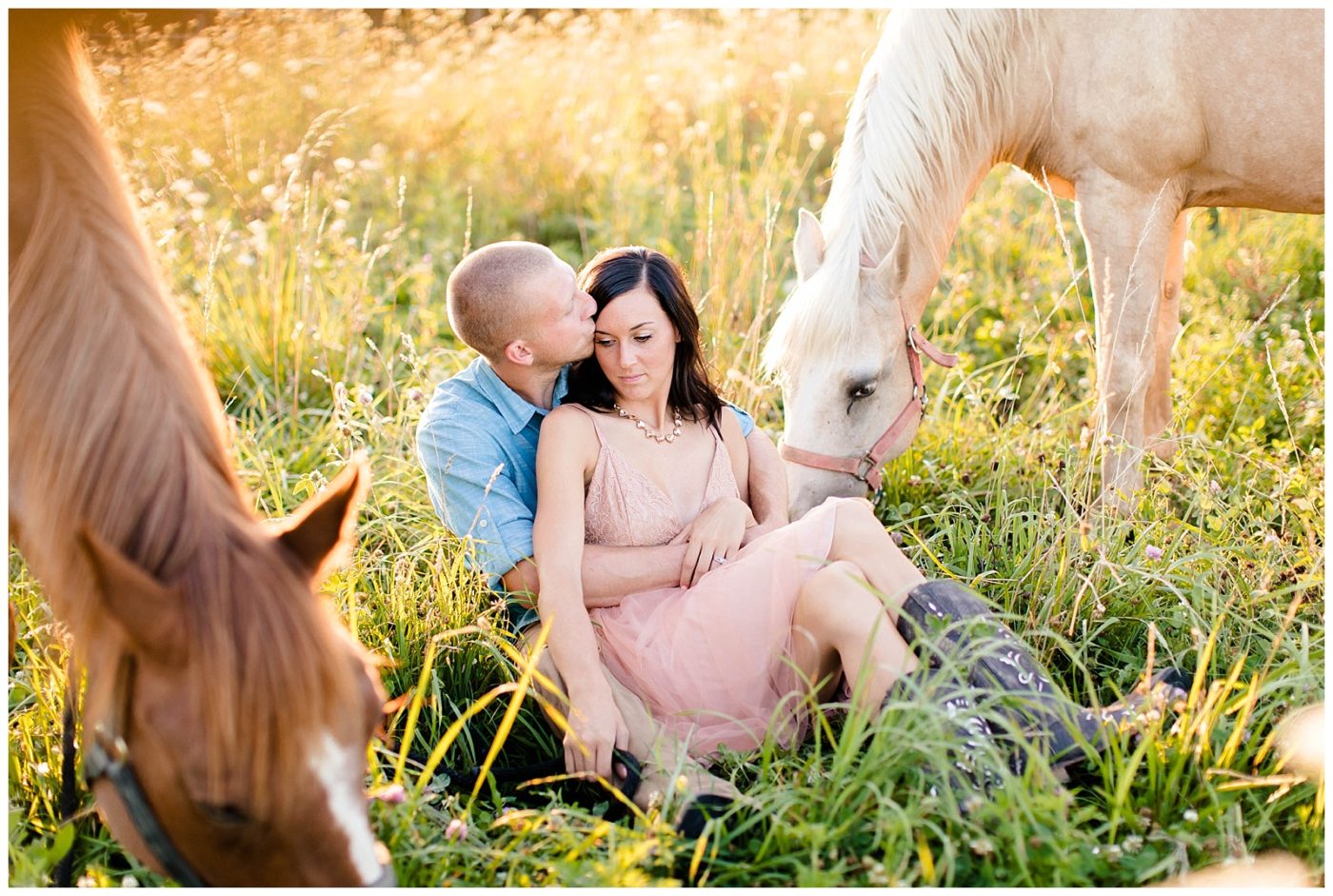 Couple sitting in a field with their horses on grazing beside them for their photos 