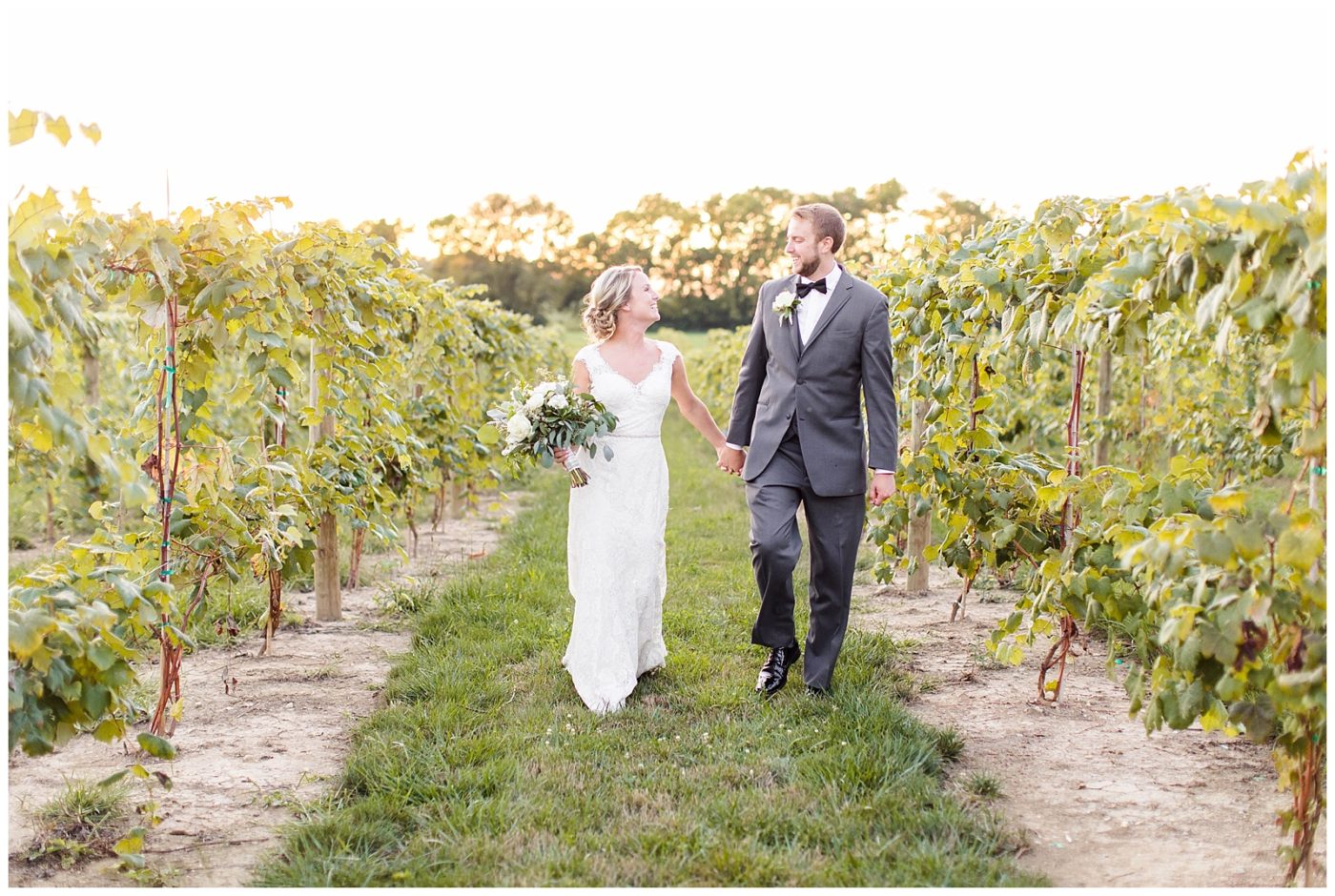 Bride and Groom holding hand and laughing with each other as they walk down the vineyard at sunset 