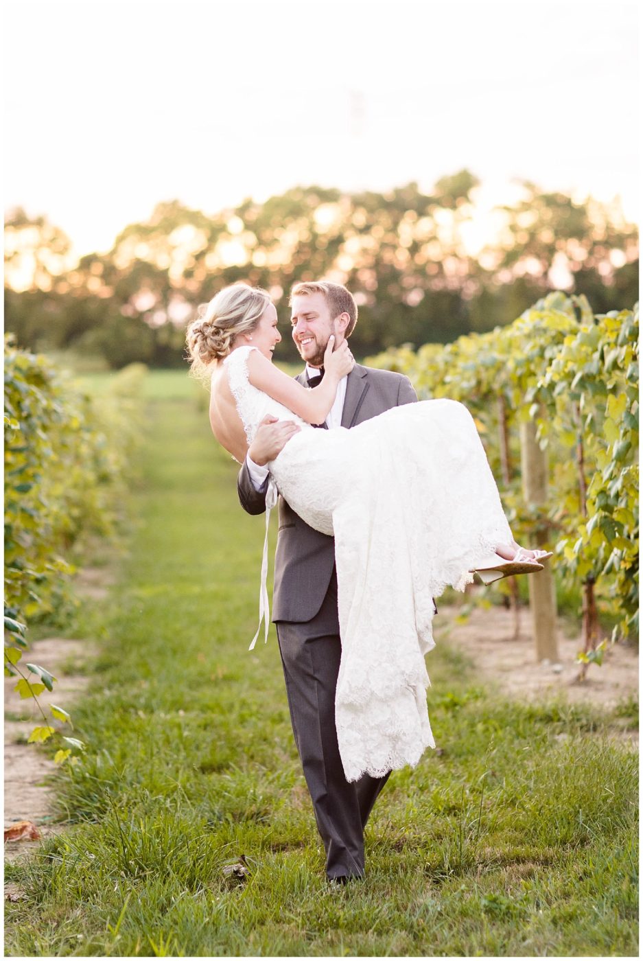 Groom gently lifting up his bride and carrying at sunset along a vineyard in Indiana. 